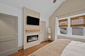Quarto com lareira, televisão na parede, espelho e janela com persianas.