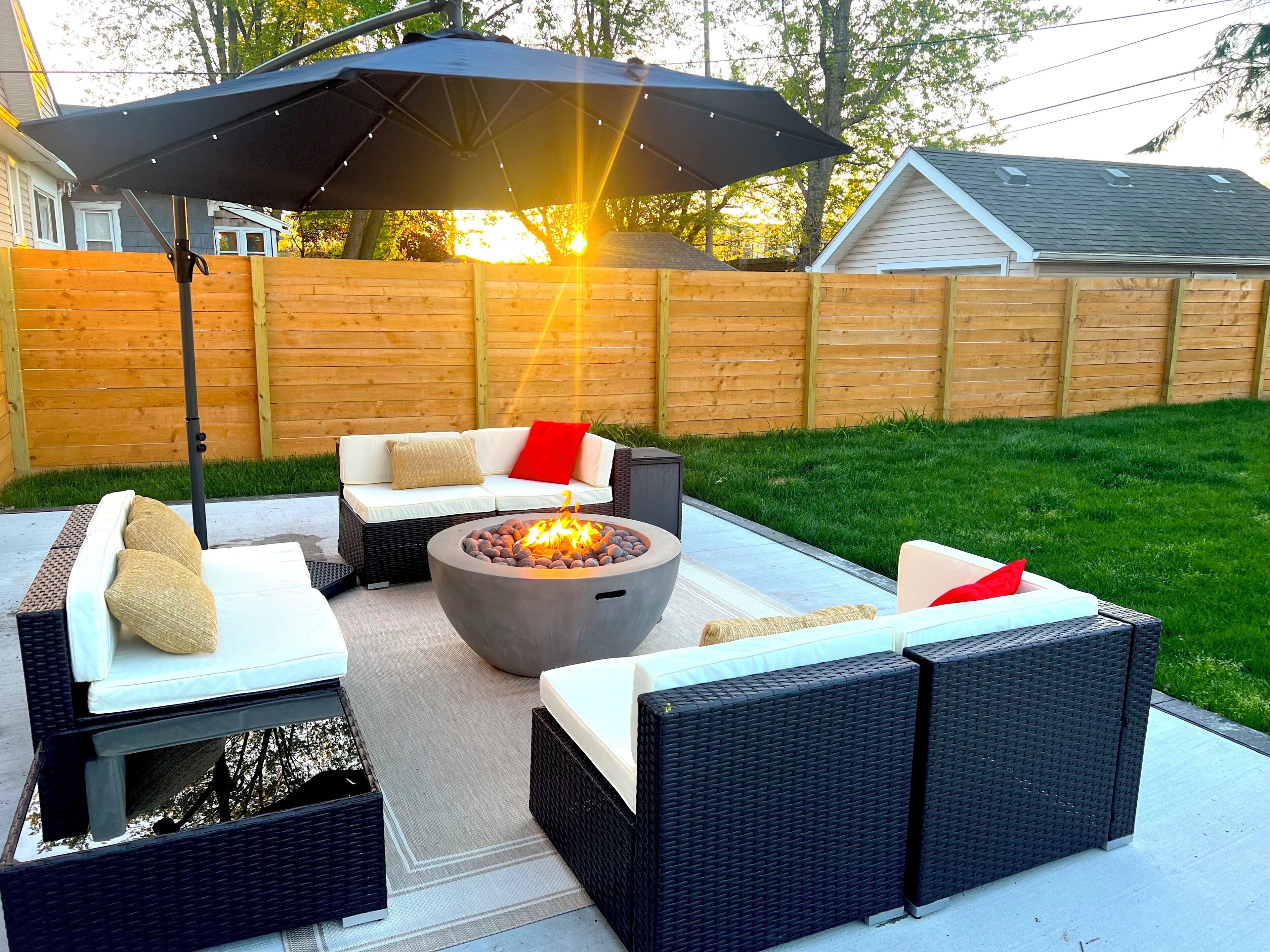 An outdoor patio with wicker furniture, a fire pit, and a large umbrella.
