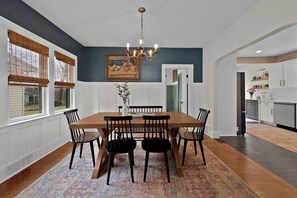 Uma sala de jantar com mesa e cadeiras de madeira, um candelabro e um quadro na parede.