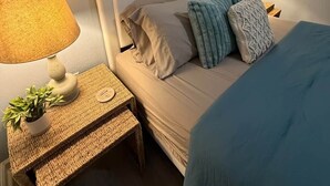 Ein Hotelzimmer mit einem Bett, zwei Nachttischlampen, einem kleinen Tisch mit Pflanze und einem an der Wand hängenden Kunstwerk.