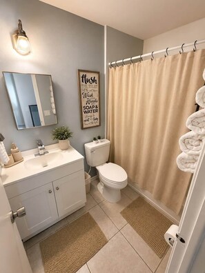 Un bagno con un lavandino bianco, un water, una tenda da doccia, uno specchio e un cartello fissato al muro.