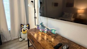 Ein Zimmer mit einem Holzkleiderschrank, einem großen Flachbildfernseher an der Wand, einem Plüschtier und einer dekorativen leuchte in Fischform.