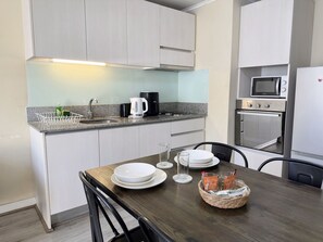 A modern kitchen with a granite countertop, stainless steel appliances, and a dining area with a wooden table and chairs. - Oceana Suites Alberto Hurtado (Estación Central)
