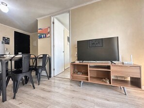 A modern living room with a flat-screen TV, wooden entertainment unit, and a dining area with a table and chairs. - Oceana Suites Alberto Hurtado (Estación Central)
