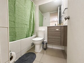 Une petite salle de bain compacte, équipée de toilettes, d’une poubelle et d’un rideau de douche.