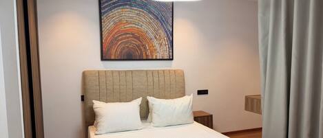 Quarto de hotel com uma cama grande, cabeceira, mesa de cabeceira, obra de arte na parede e luminária moderna.