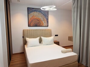 Habitación de hotel con una cama grande, un cabecero, una mesita de noche, una obra de arte en la pared y un accesorio de iluminación moderno.