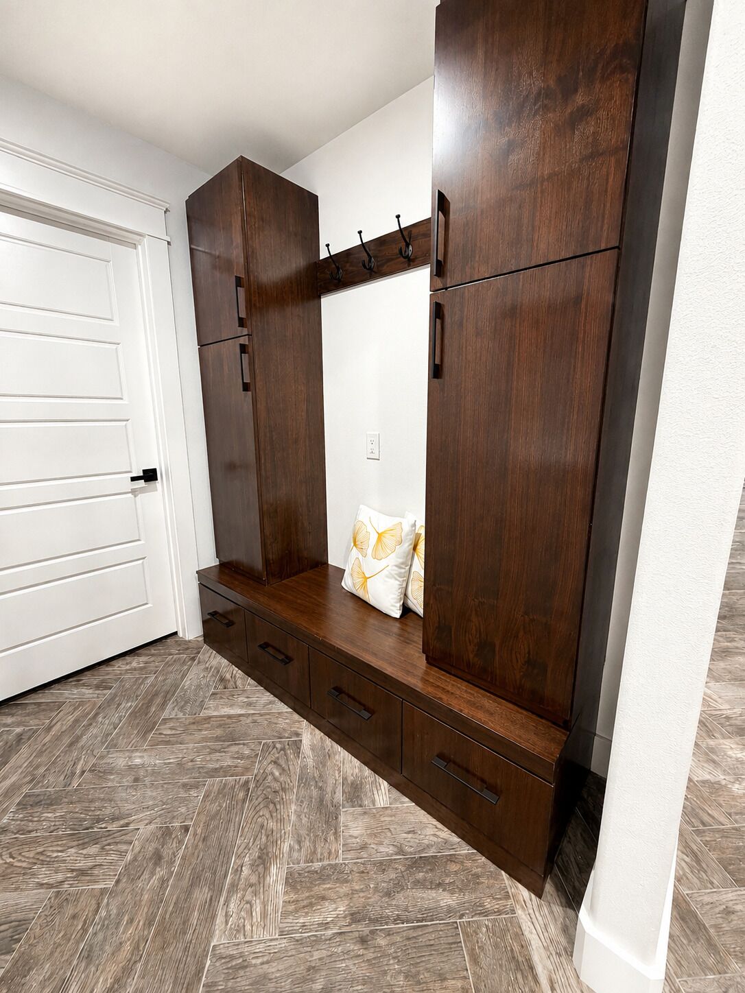 A room with a built-in wardrobe, a bench with cushions, and a herringbone-patterned floor.