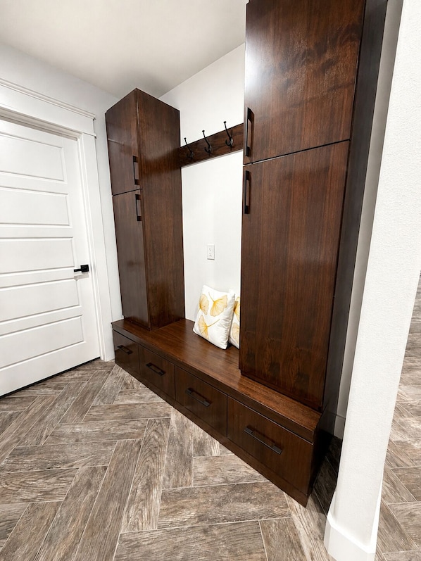 A room with a built-in wardrobe, a bench with cushions, and a herringbone-patterned floor.