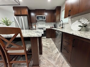 A modern kitchen with wooden cabinets, stainless steel appliances, and a marble countertop.