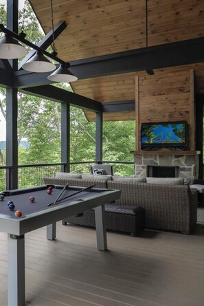 Une table de billard avec des billes, un téléviseur fixé à un mur en pierre et un coin salon avec des coussins.