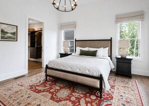A bedroom with a large bed, a nightstand with a lamp, a window with a view, and a walk-in closet. - Modern Mountain View Cabin w Expansive Deck close to Cashiers (Glenville)