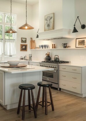 A kitchen with a central island, bar stools, a stove, and hanging pendant lights. - Modern Mountain View Cabin w Expansive Deck close to Cashiers (Glenville)