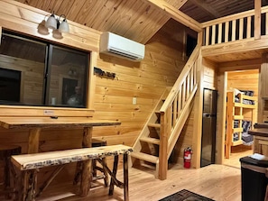 L’intérieur d’un chalet en bois comprend une table à manger, un banc, un escalier et un réfrigérateur.
