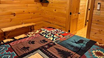 A wooden cabin interior with a bed, a bench, and a door leading outside.