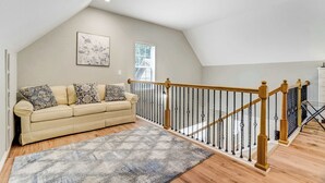 A loft-style living room with a high ceiling, a wooden staircase with black balusters, a beige sofa with patterned cushions, and a large window with blinds. - Ponderosa Woods! Forest Hot Tub Escape by Monument (Monument)