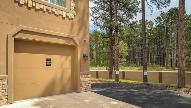 A building with a garage door, a 'NO PARKING KEEP DRIVEWAY CLEAR' sign, and a 'WELCOME GUEST PARKING' sign. - Ponderosa Woods! Forest Hot Tub Escape by Monument (Monument)