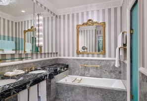 Casa de banho com duas pias, banheira e um espelho grande com moldura dourada.