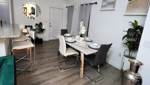 Uma área de refeições moderna com uma mesa de madeira posta para quatro pessoas, um espelho acima da mesa e uma planta ao lado.