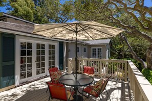 Un espacio al aire libre cubierto con una mesa y sillas, una cerca blanca y una casa con porche.