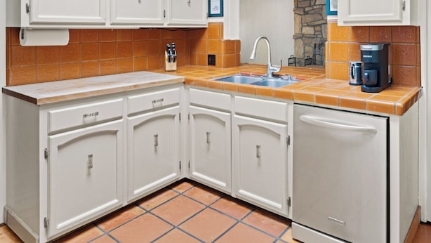 Cocina compacta con armarios blancos, un lavamanos integrado y una cafetera.