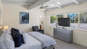 Un dormitorio con una cama, televisor, cómoda y ventilador de techo.