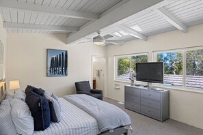 A bedroom with a bed, a television, a dresser, and a ceiling fan.