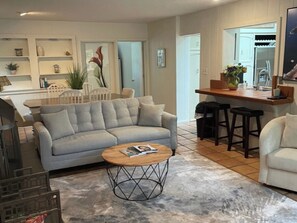 A living room with a grey sofa, a coffee table, and a kitchen area with a counter and stools.