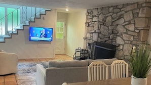 Una sala de estar con chimenea de piedra, televisor montado en la pared y una escalera que lleva a otro nivel.