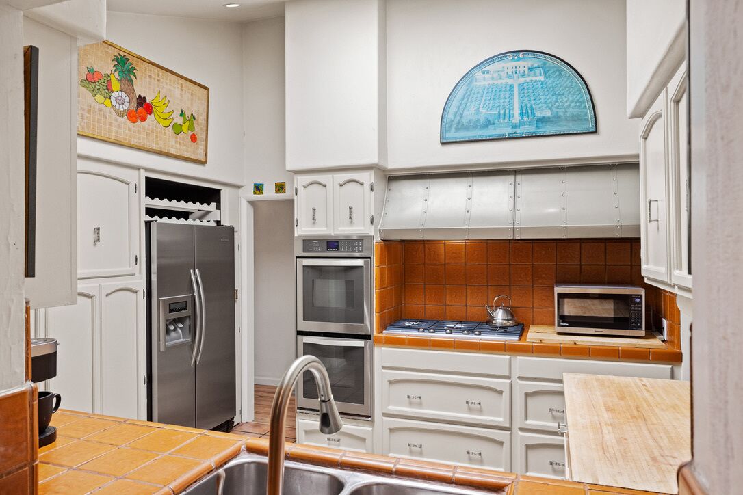 A kitchen with white cabinets, a stainless steel refrigerator, an oven, a microwave, and a sink.