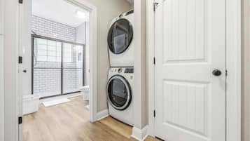 A laundry room with two stacked front-loading washing machines, a shower area with a glass door, and a white door leading to another room.