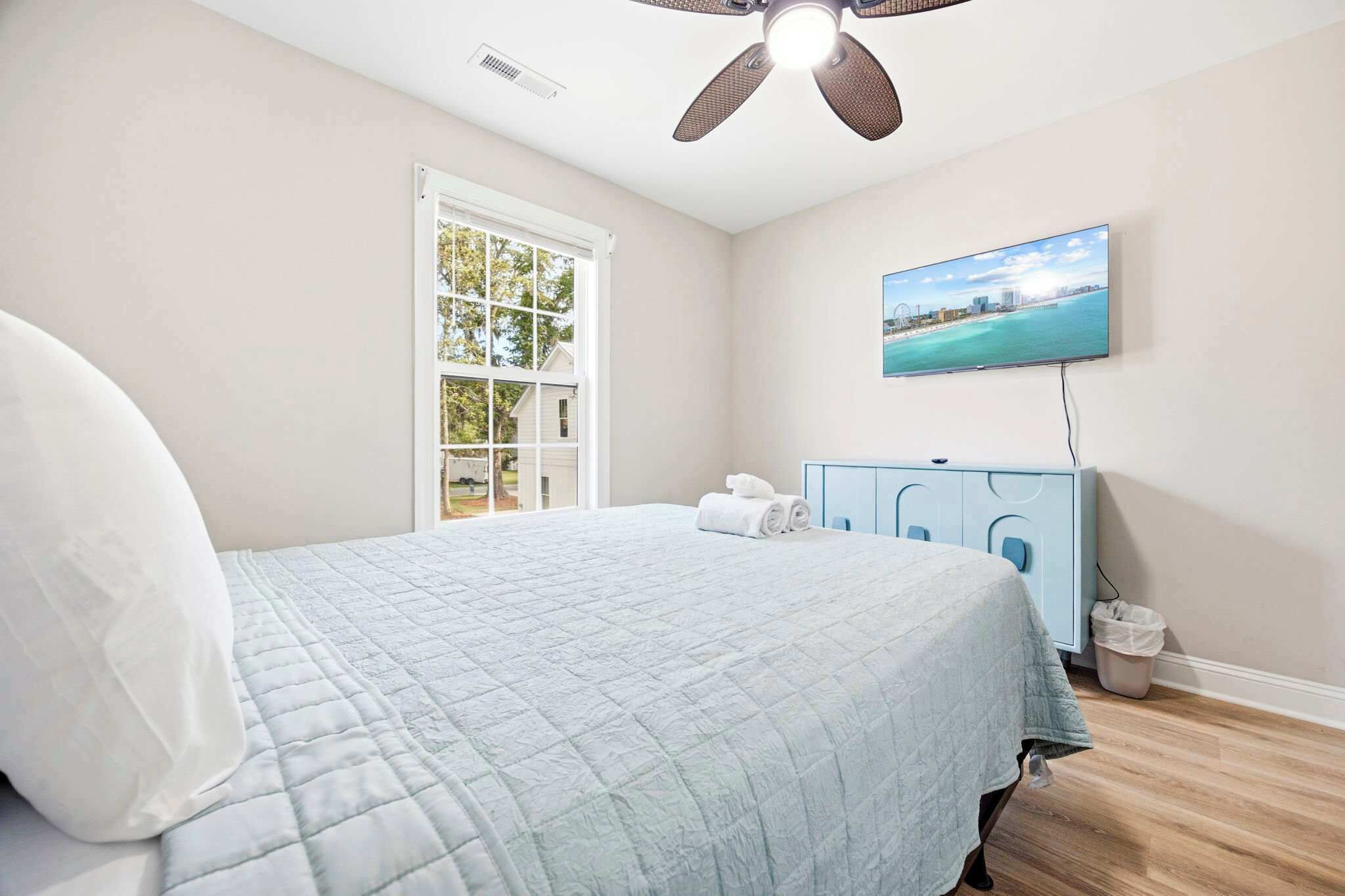A bedroom with a bed, a window, a ceiling fan, a TV, and a dresser.