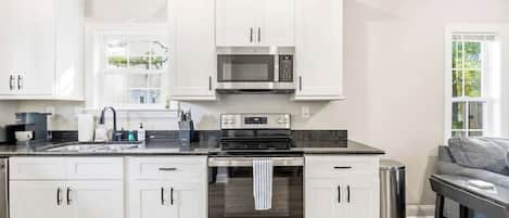 Una cocina moderna con armarios blancos, microondas integrado, estufa y lavaplatos.