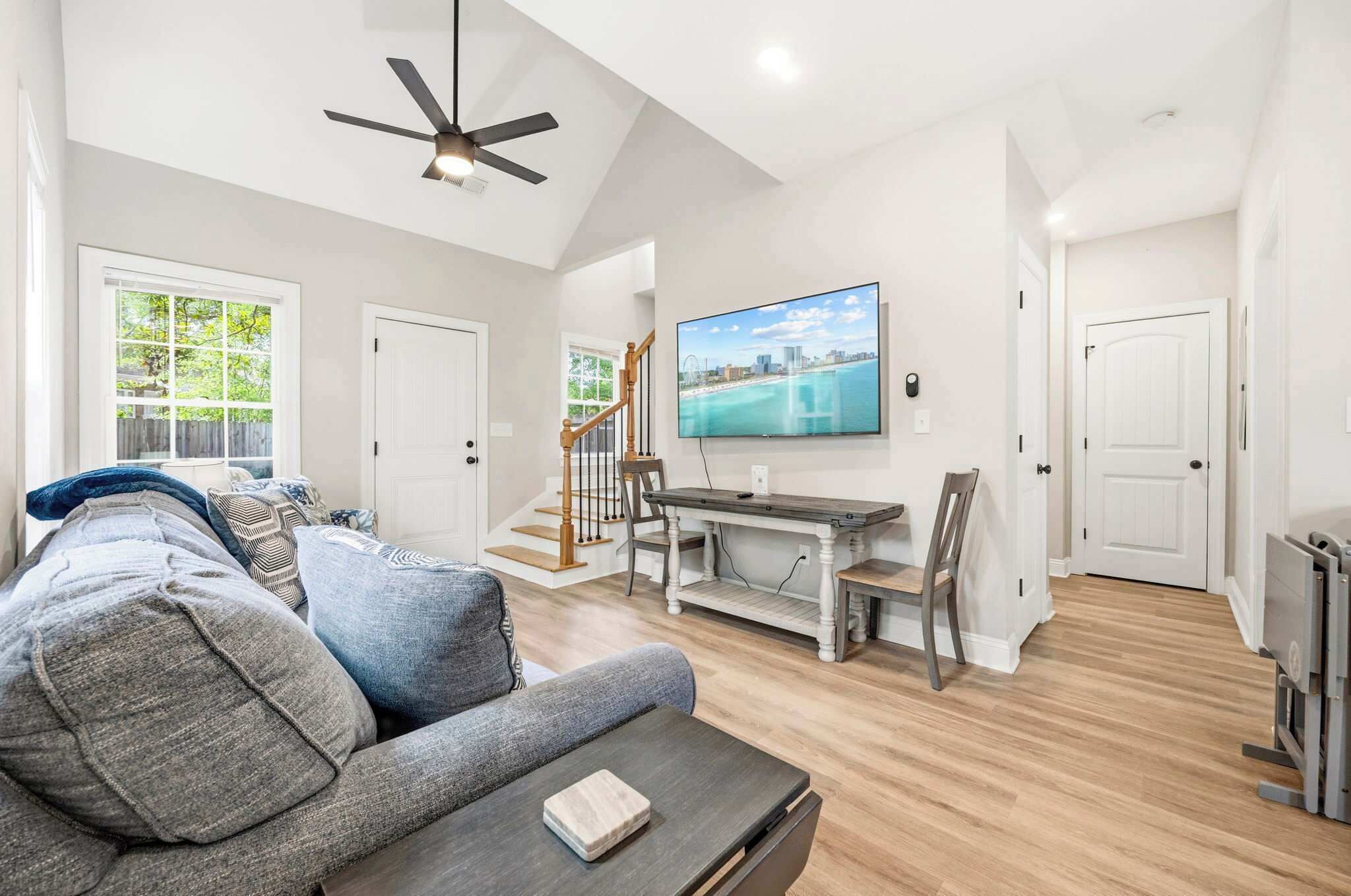 A spacious living room with a gray sofa, a coffee table, and a TV mounted on the wall.
