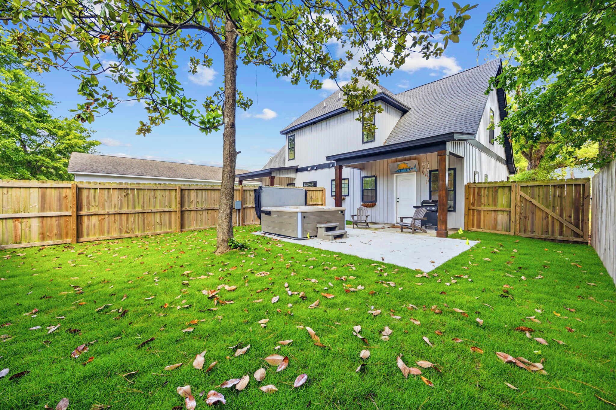 A backyard with a hot tub, barbecue grill, and a covered patio area.