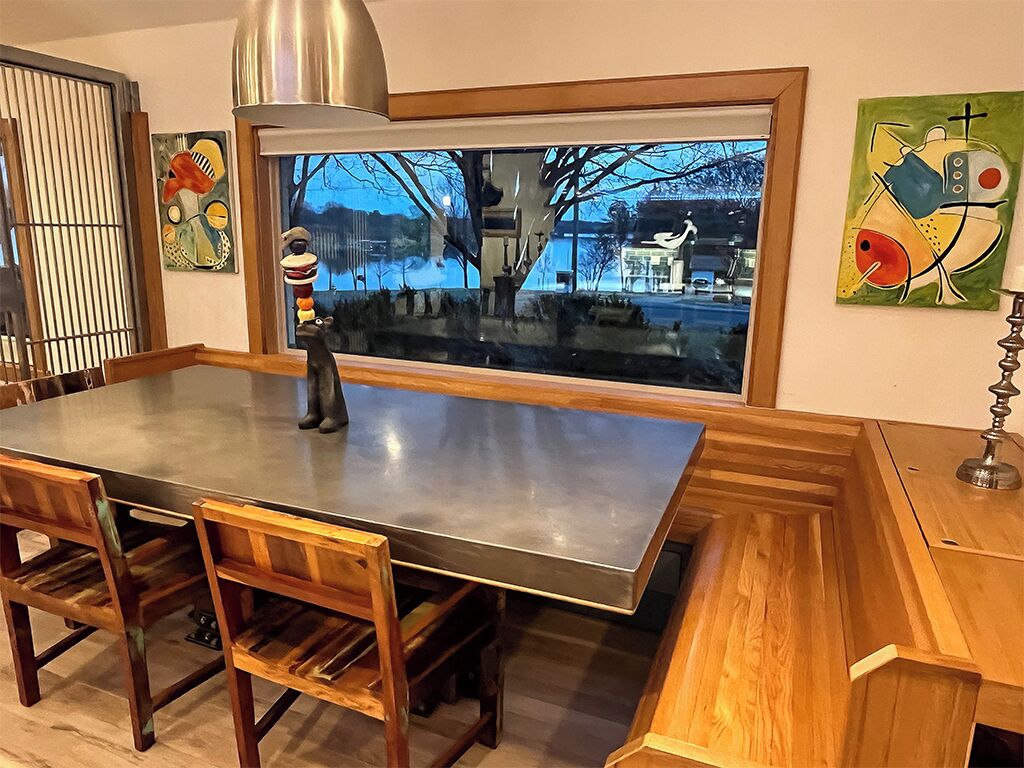 A modern kitchen with a large island, wooden chairs, and a view of a cityscape through a large window.
