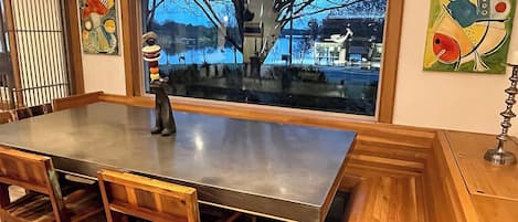 A modern kitchen with a large island, wooden chairs, and a view of a cityscape through a large window.