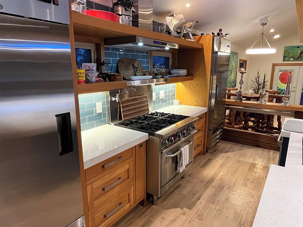 Une cuisine moderne dotée d’un réfrigérateur en acier inoxydable, d’une cuisinière à gaz, de meubles en bois et d’un plan de travail blanc.