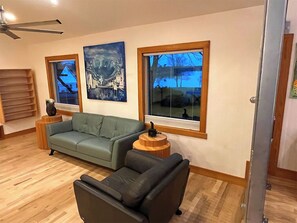Uma sala de estar com sofá seccional, uma poltrona preta, uma mesinha de madeira e duas obras de arte emolduradas na parede.