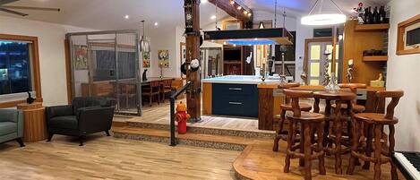 A modern kitchen with a central island, wooden bar seating, and a view of the city at night.