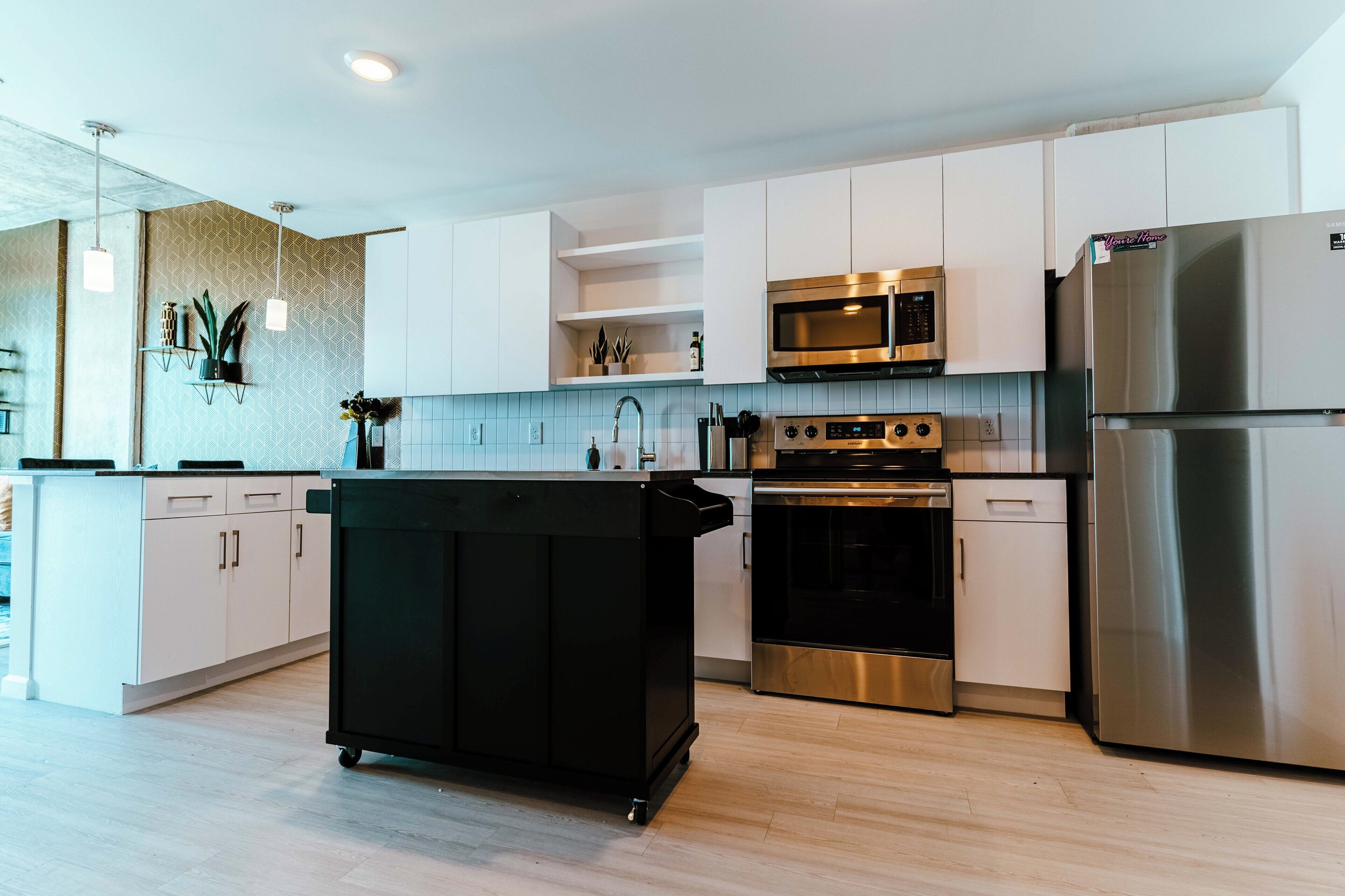 Una cocina moderna con armarios blancos, electrodomésticos de acero inoxidable y un carrito negro.