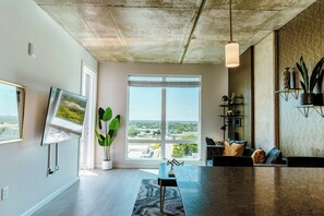 Un salon moderne doté d’une grande fenêtre, d’un téléviseur à écran plat et d’un coin repas avec une table en marbre.