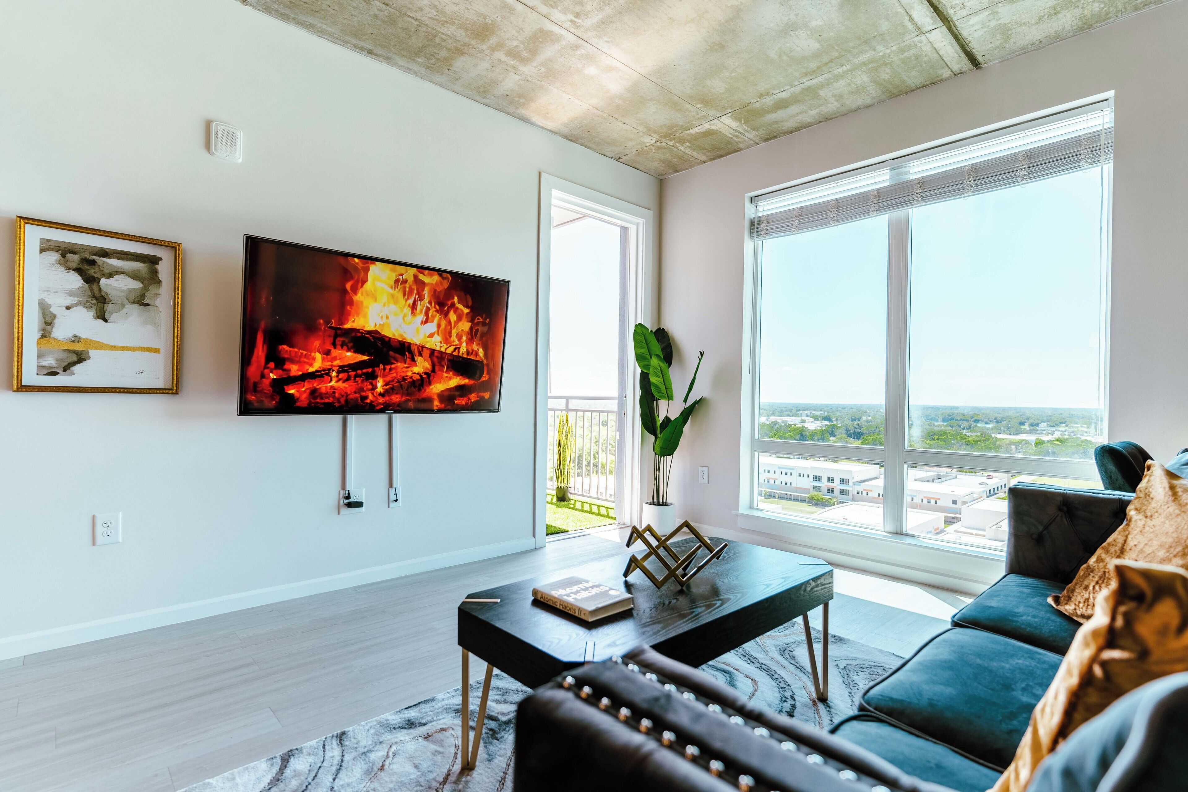 Una sala moderna con un televisor de pantalla plana, un sofá, una mesa de centro y vistas a la ciudad a través de amplios ventanales.