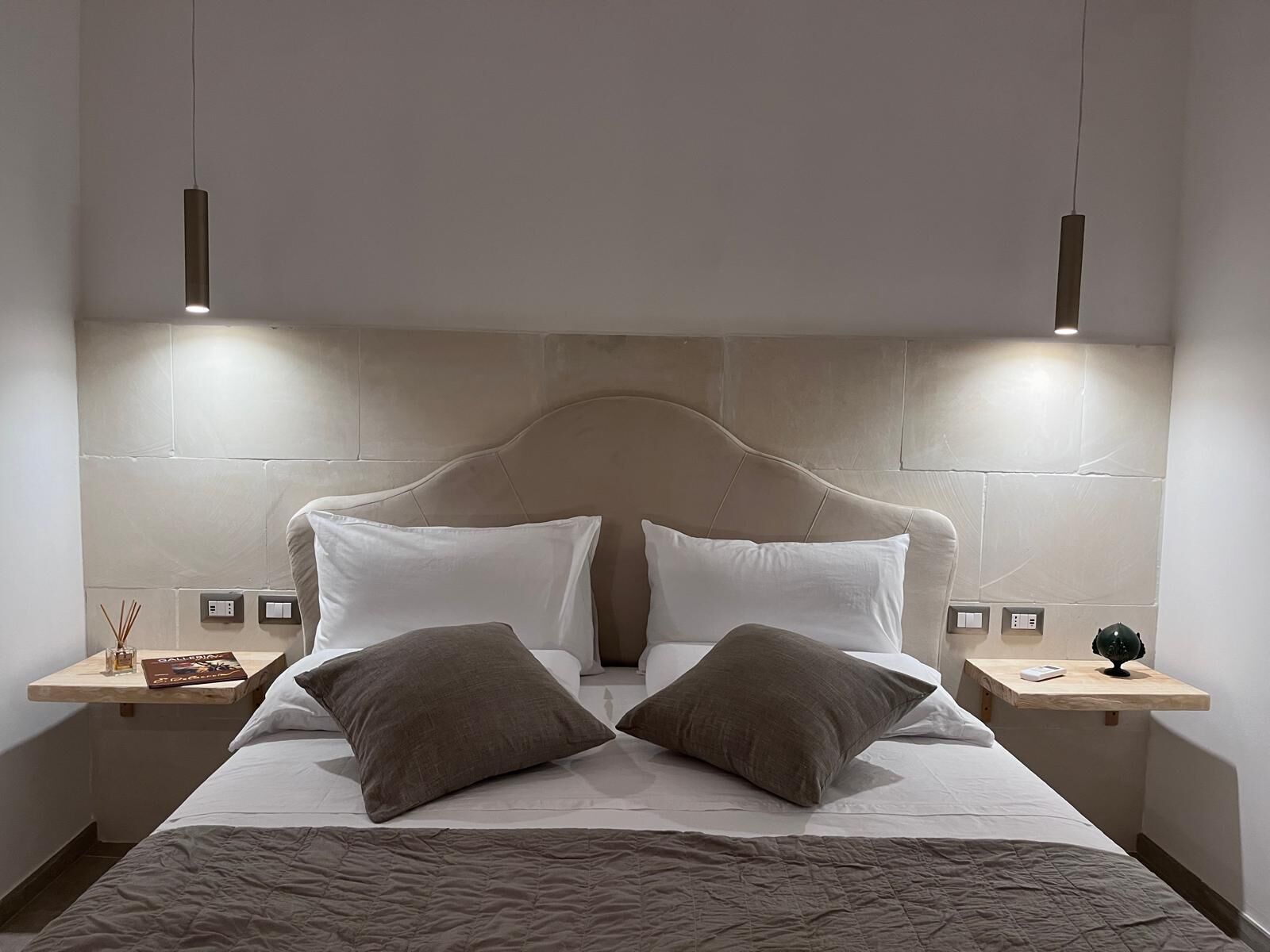 A modern hotel room with a large bed, two bedside tables, and a headboard.