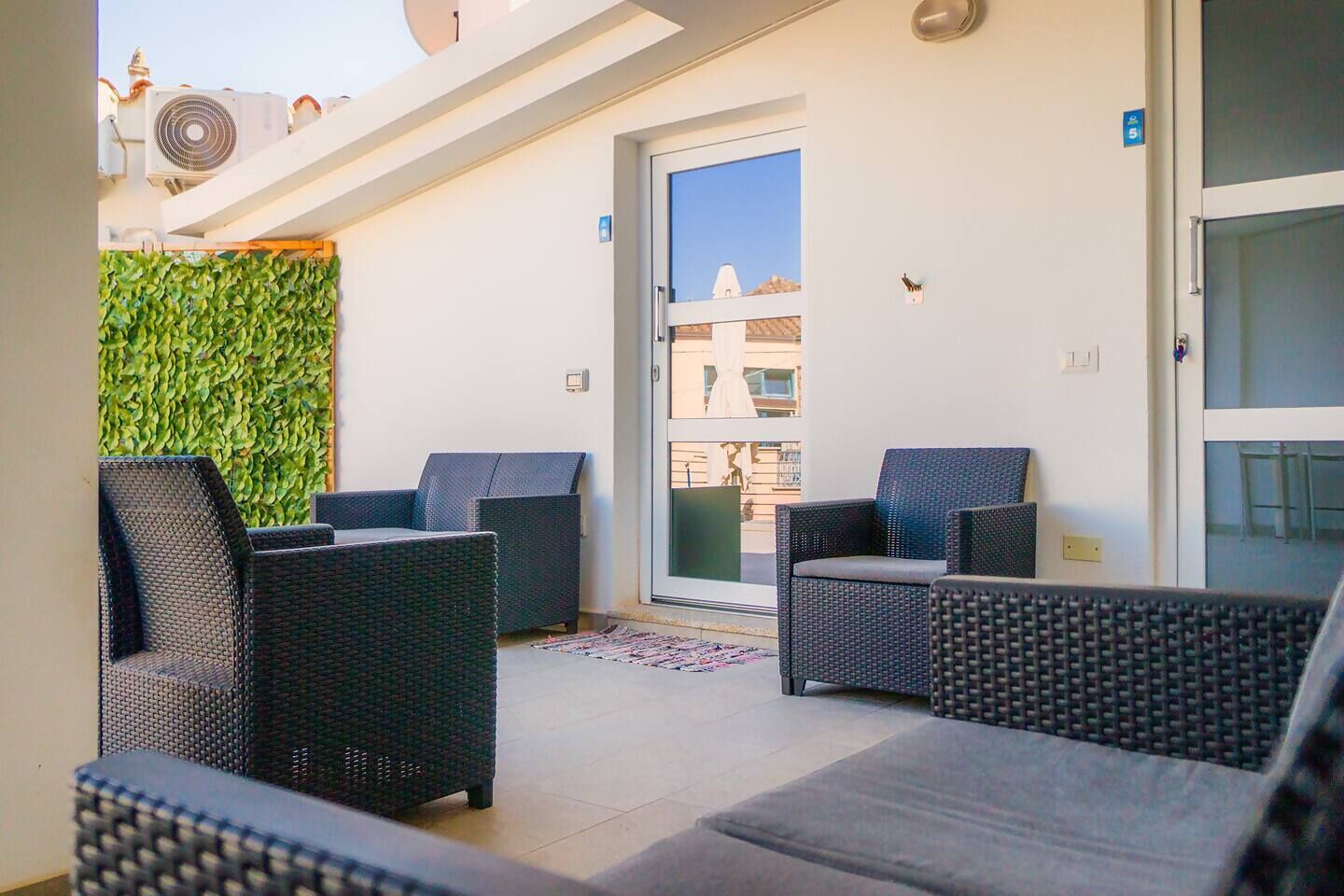 A balcony with wicker furniture, a green wall, and a clear view of buildings in the background.