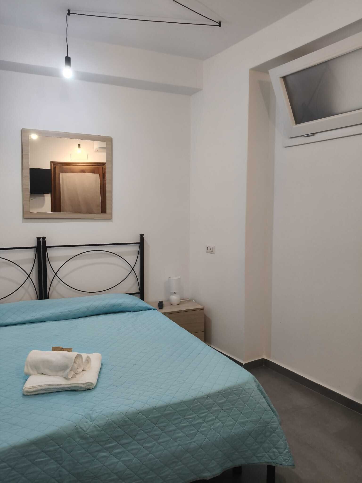 A bedroom with a bed, a bedside table, a mirror, and a TV mounted on the wall.