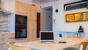 Cozinha moderna com forno embutido, mesa de jantar com cadeiras e um laptop sobre a mesa.
