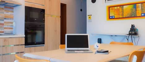 A modern kitchen with a built-in oven, a dining table with chairs, and a laptop on the table.