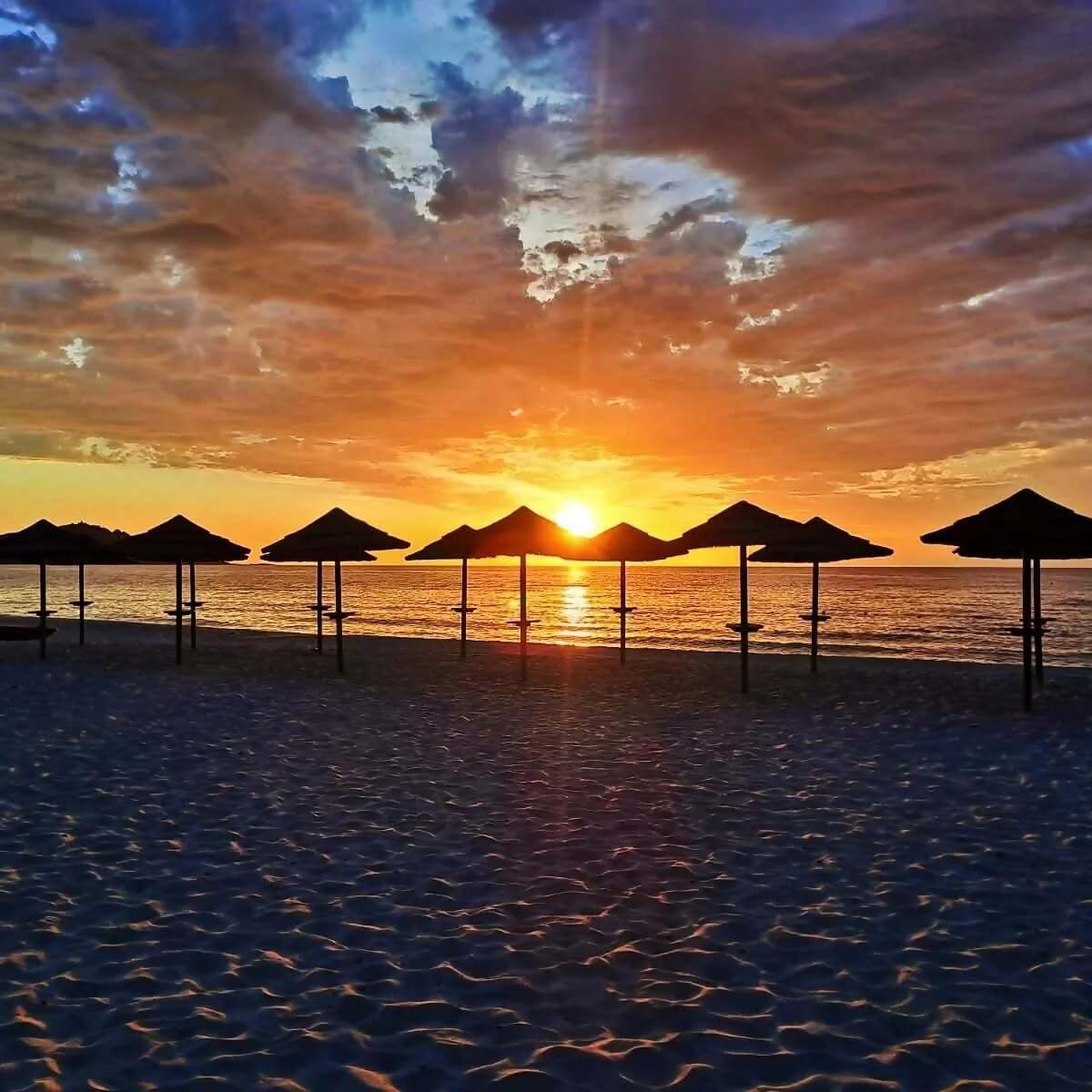 Ein Strand mit Sonnenschirmen und einem Sonnenuntergang.