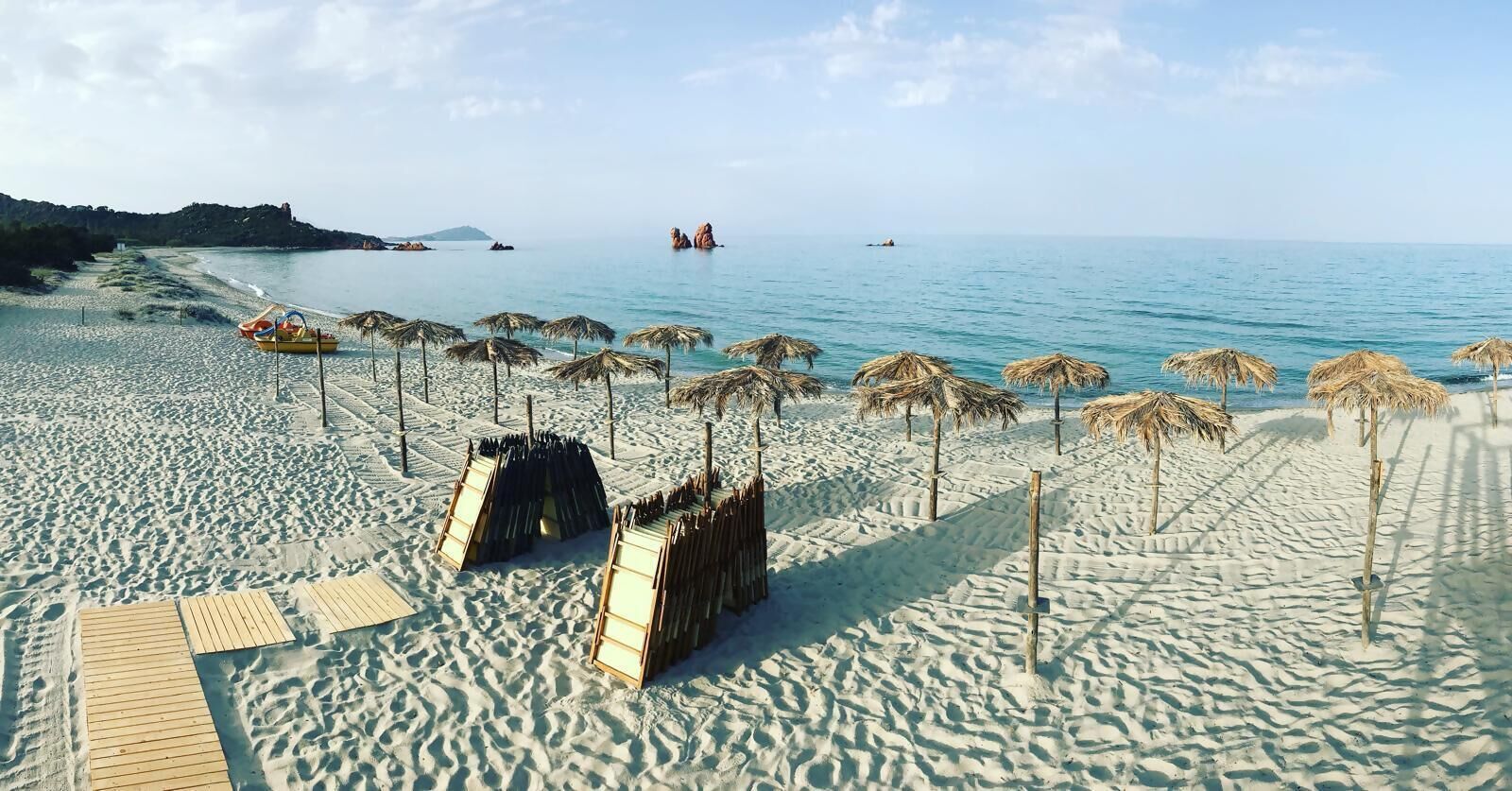 A beach with umbrellas, a wooden walkway, and a clear view of the sea.